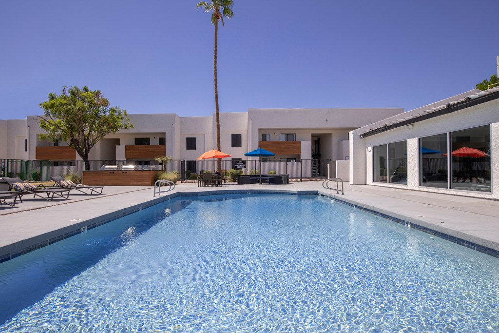 a large swimming pool with lounge chairs and umbrellas in front of a white building