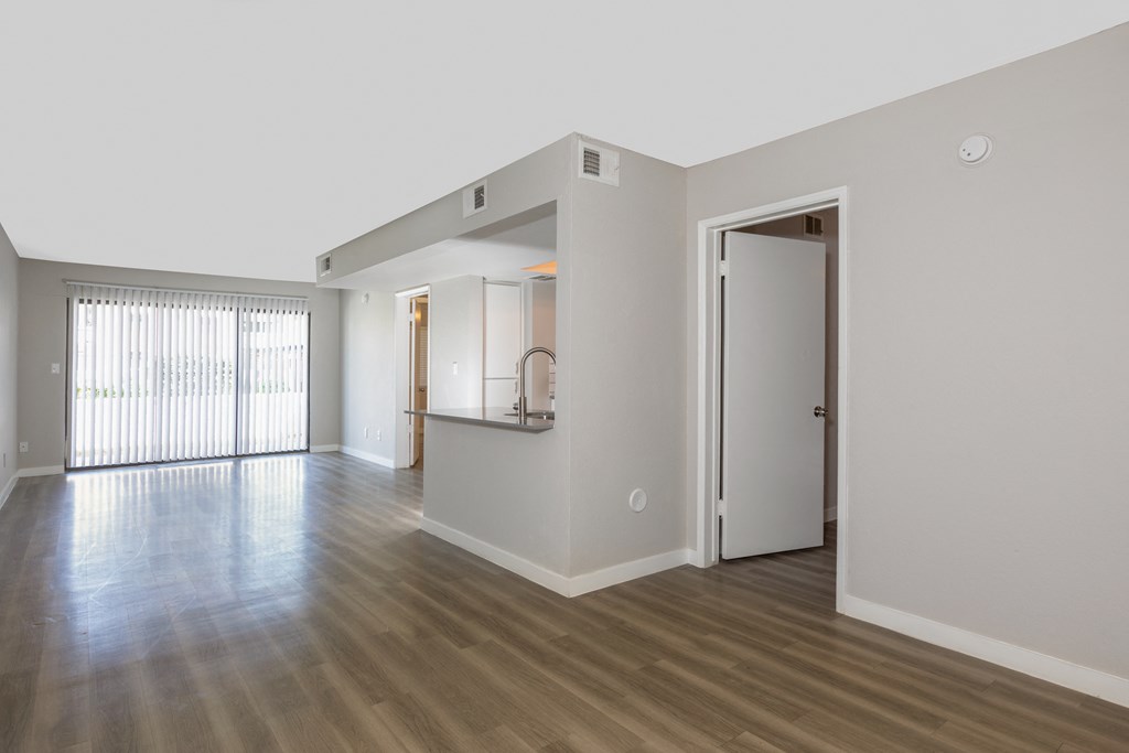 an empty living room and kitchen with wood floors and white walls