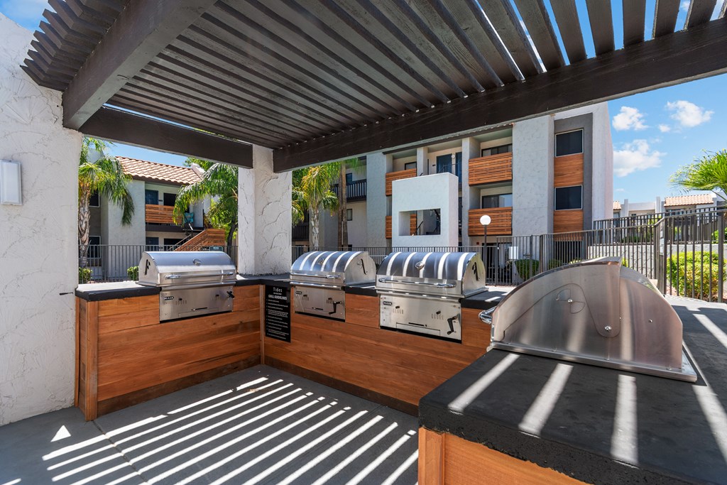 a covered patio with three bbq grills and a building in the background