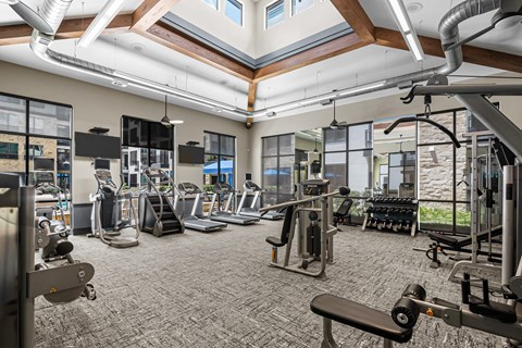 a gym with cardio equipment and weights in a building with windows