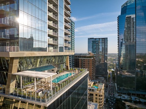 A modern building with a pool on the roof overlooks a busy street.