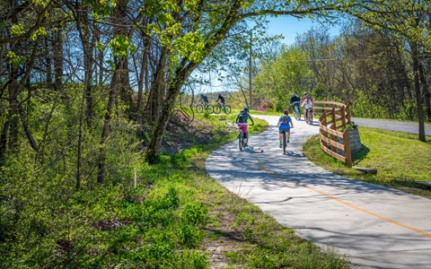 A group of people riding bikes on a paved trail in a wooded area.