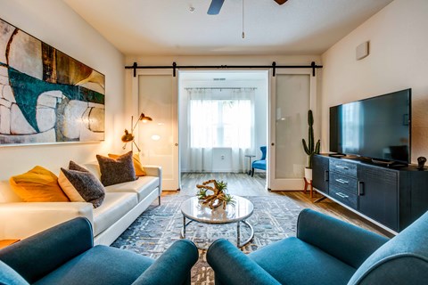 A living room with a white couch, blue chairs, and a painting on the wall.