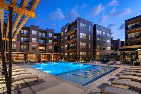 A swimming pool surrounded by sun loungers and apartment buildings.