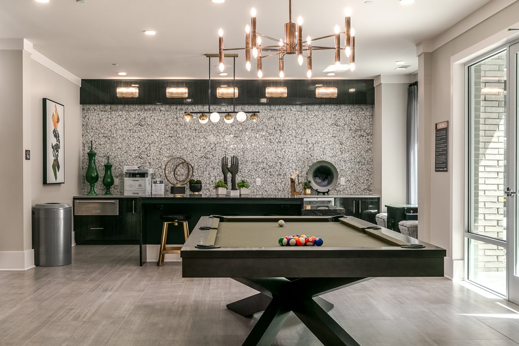 A pool table is in the middle of a room with a black and white tiled wall behind it.