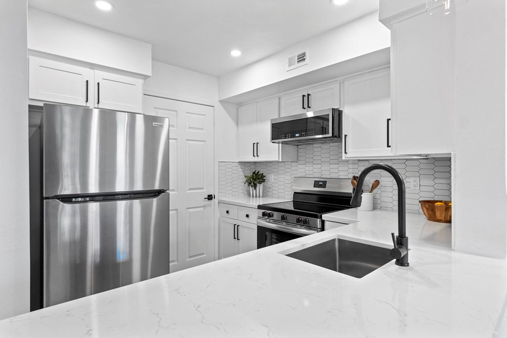 a white kitchen with stainless steel appliances and a sink
