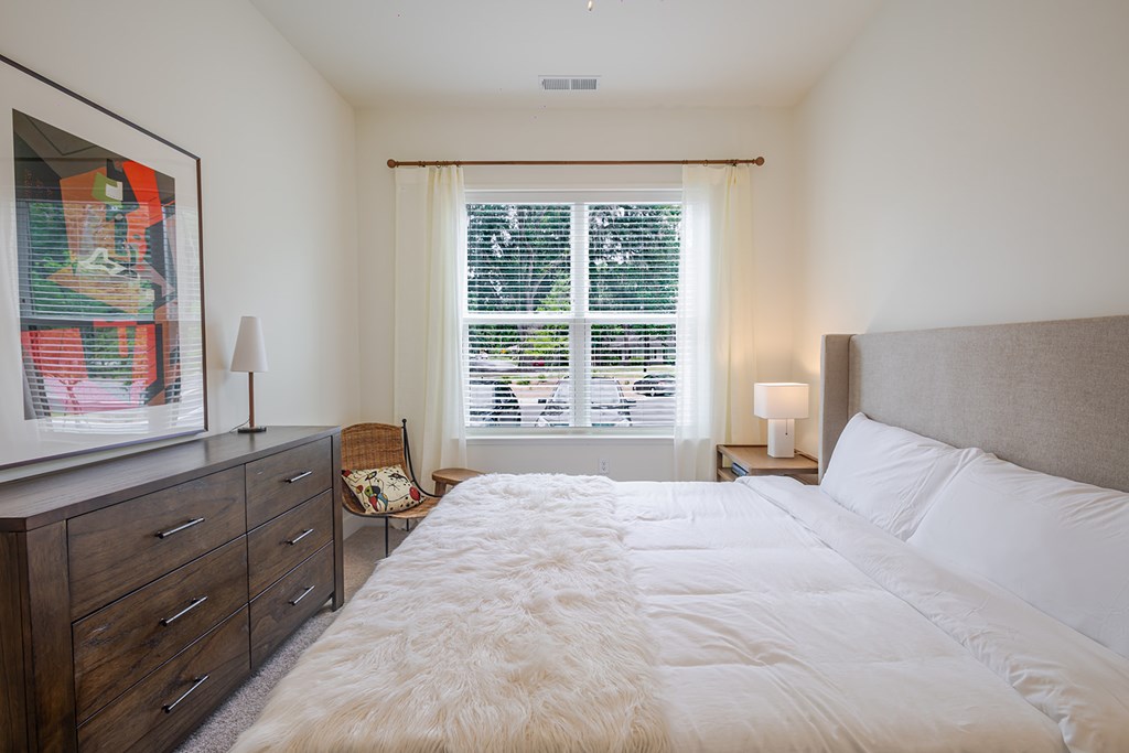 A bedroom with a large bed, a dresser, and a window with blinds.