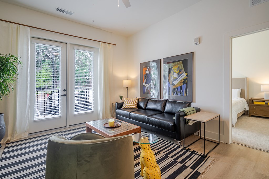 A living room with a black leather couch and a yellow vase on the coffee table.