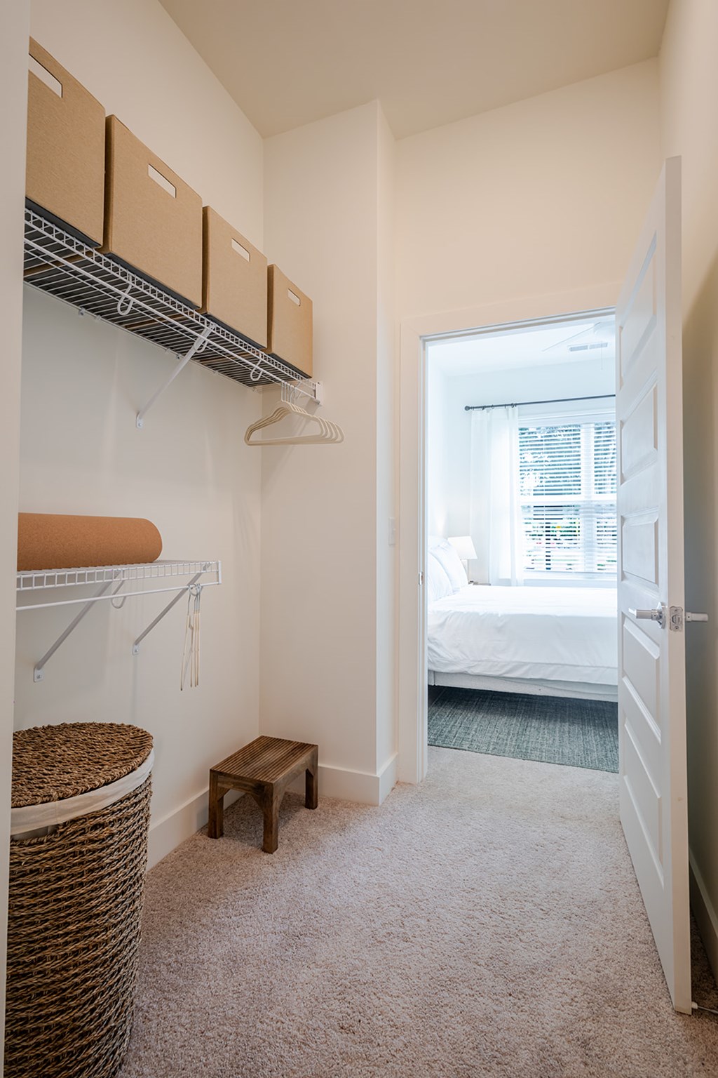 A room with a white wall and a bed in the background.