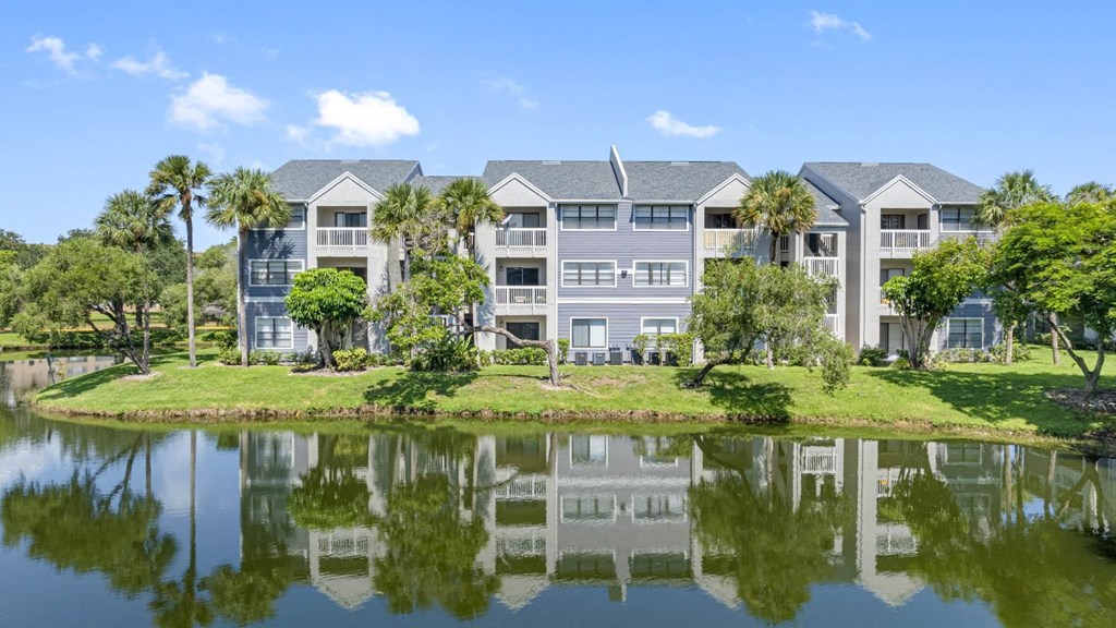 A large building with a grey facade is reflected in a body of water.