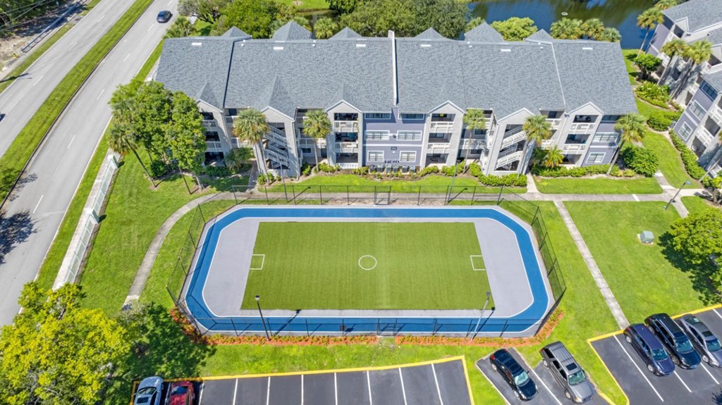 A soccer field is surrounded by a parking lot and apartment buildings.