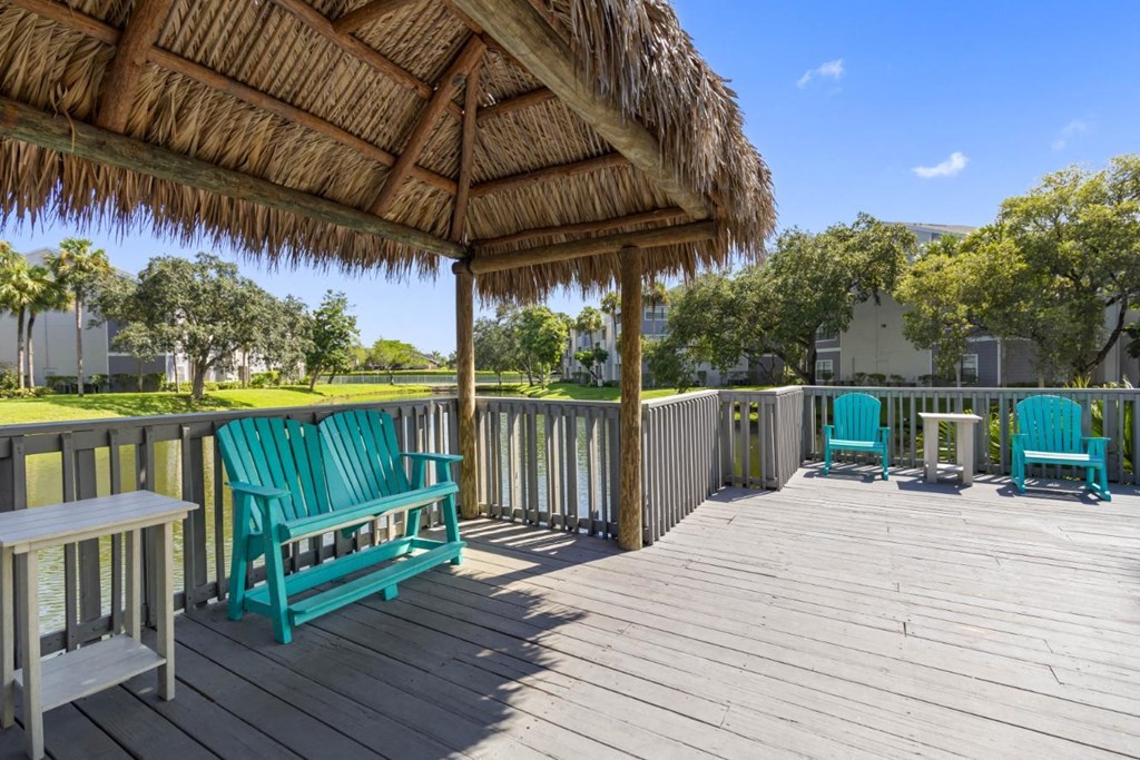 a covered porch with white chairs and a bar on the water