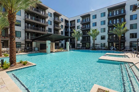 A large swimming pool in front of a multi-story apartment building.