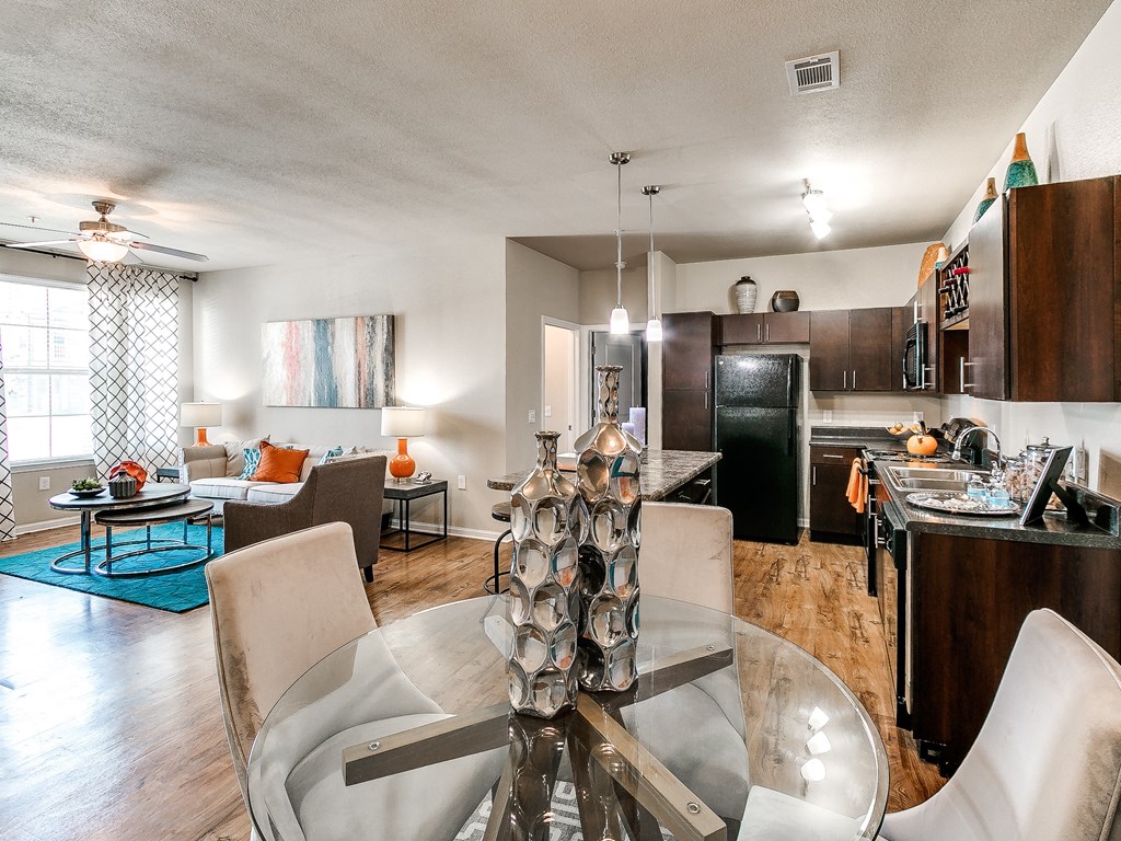 a living and dining room area with a glass table and chairs and a kitchen in the background