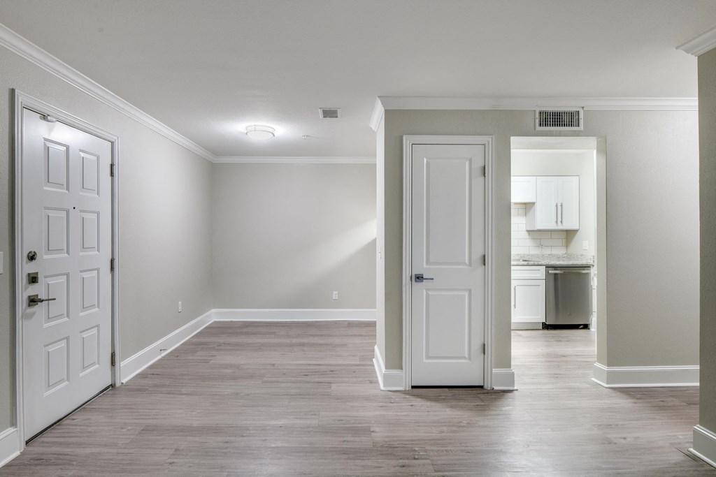 an empty living room with white doors and a hallway to a kitchen