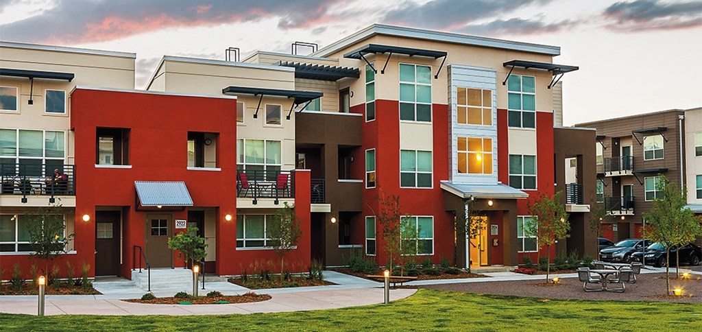 a group of apartment buildings with a green lawn and a cloudy sky