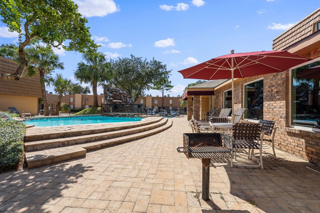 a patio with chairs and umbrellas next to a pool