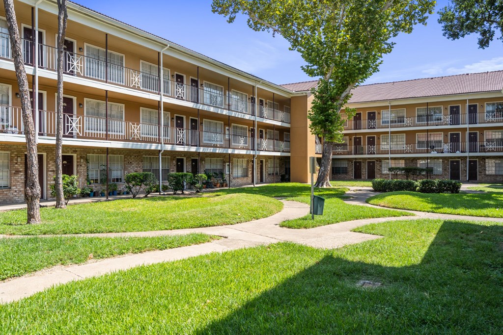 a grassy area with trees and a walkway in front of an apartment building