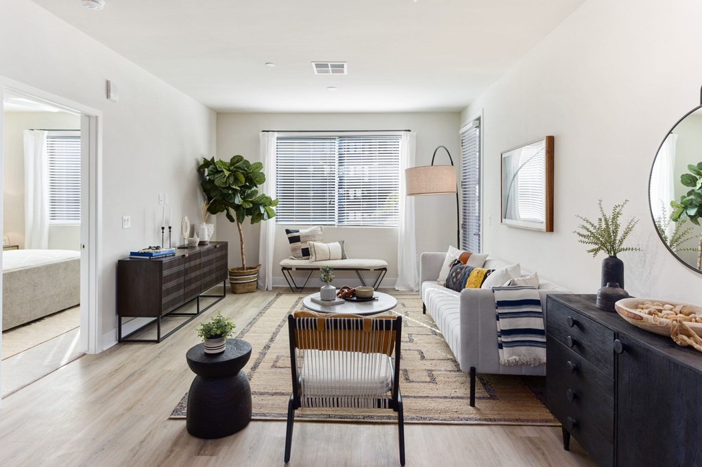 A modern living room with a grey sofa, a wooden coffee table, and a large mirror on the wall.