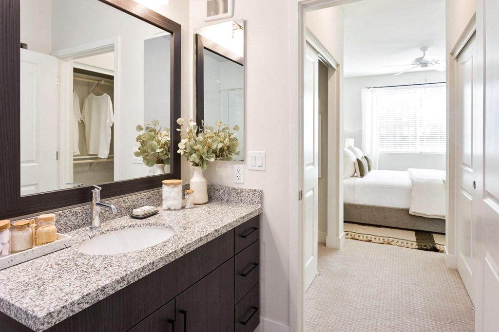 A bathroom with a sink, mirror, and a bedroom in the background.