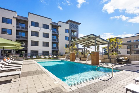 A swimming pool surrounded by lounge chairs and umbrellas in front of a modern apartment building.