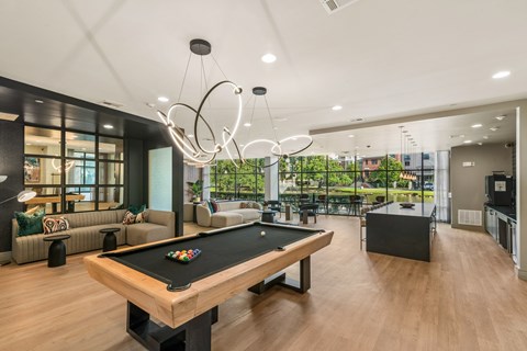 A pool table is in the middle of a room with a kitchen in the background.
