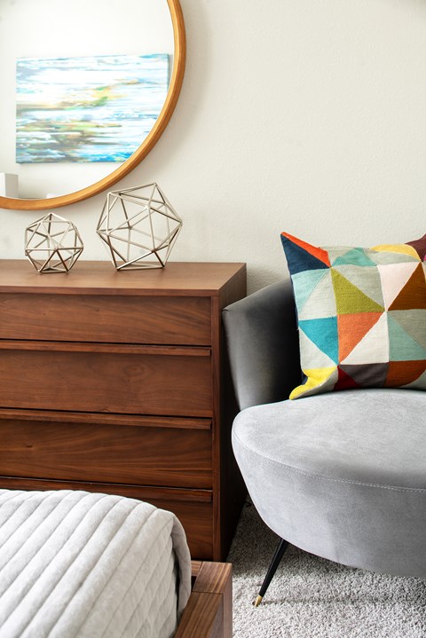 A grey couch with a pillow and a wooden dresser with a mirror above it.