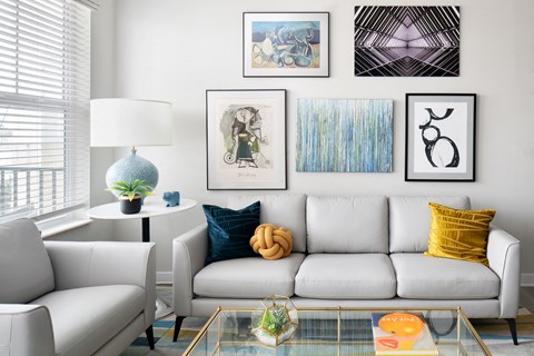 A living room with a white couch, a white chair, a glass coffee table, and a white lamp.