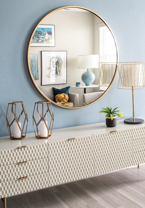 A round mirror hangs on a wall above a dresser with a patterned top.