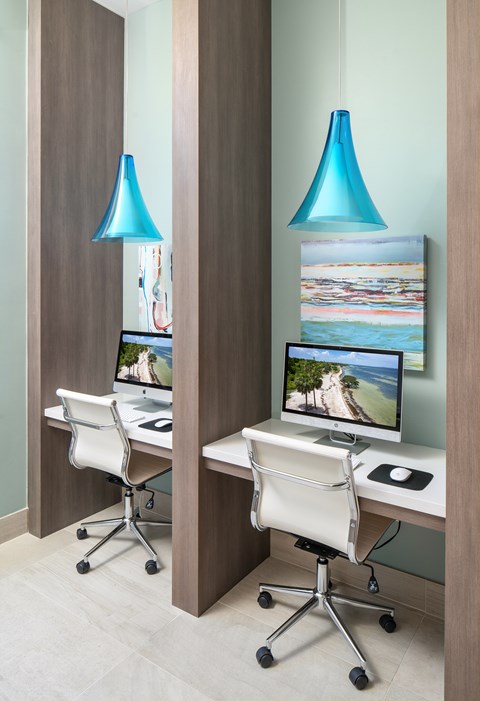 Two computers are on a desk with two blue lamps hanging from the ceiling.