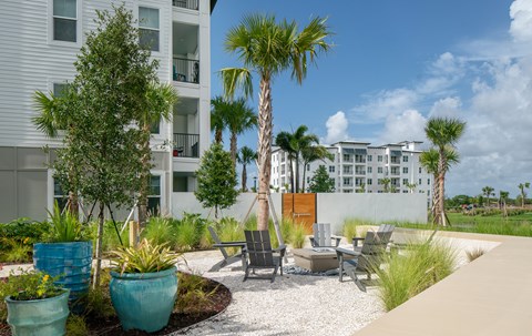 A patio area with chairs and a table surrounded by plants and trees.