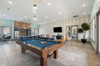 A pool table is in the middle of a room with a tv and a plant.