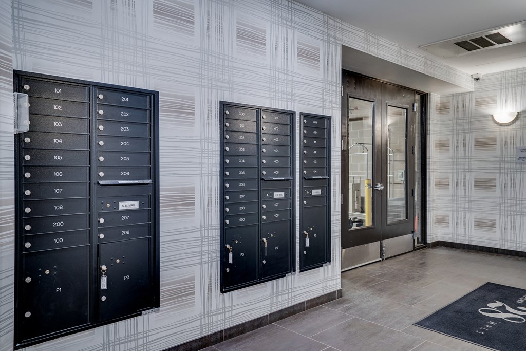 A hallway with a wall of mailboxes and a door at the end.