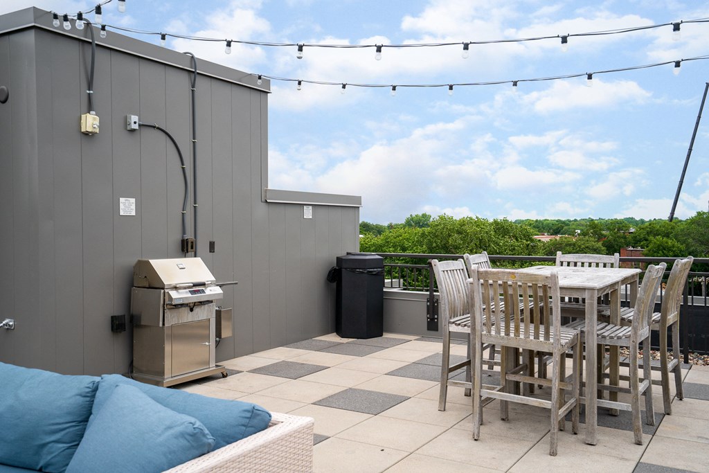 a rooftop patio with a table and chairs and a grill