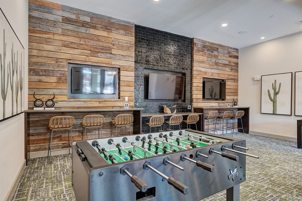 A foosball table is in the middle of a room with a wooden wall and a couch.