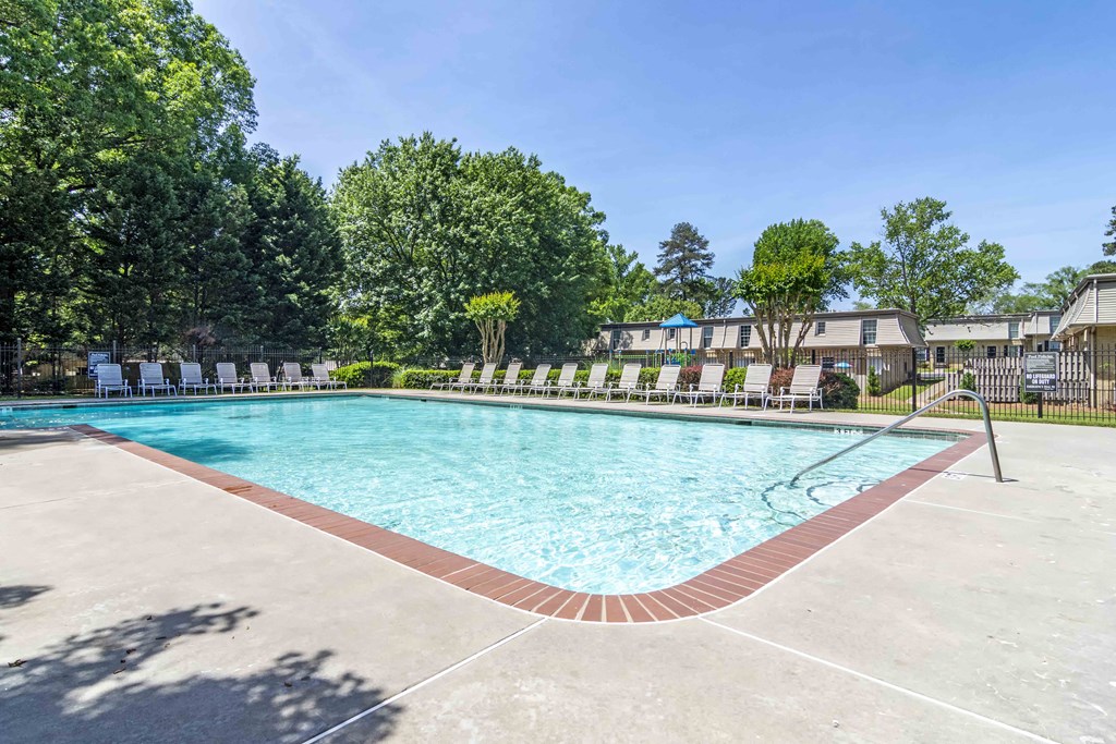 A large outdoor swimming pool surrounded by trees and a fence.