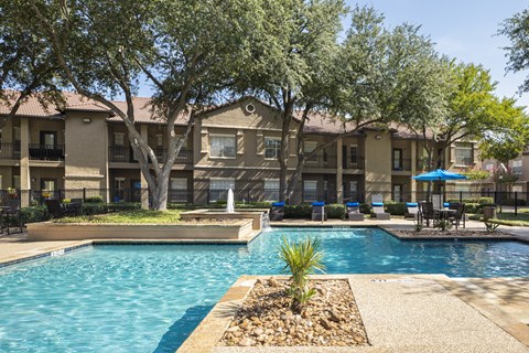 A swimming pool surrounded by trees and a building in the background.