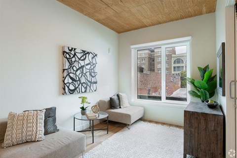 A living room with a grey couch, a coffee table, a plant, and a painting on the wall.