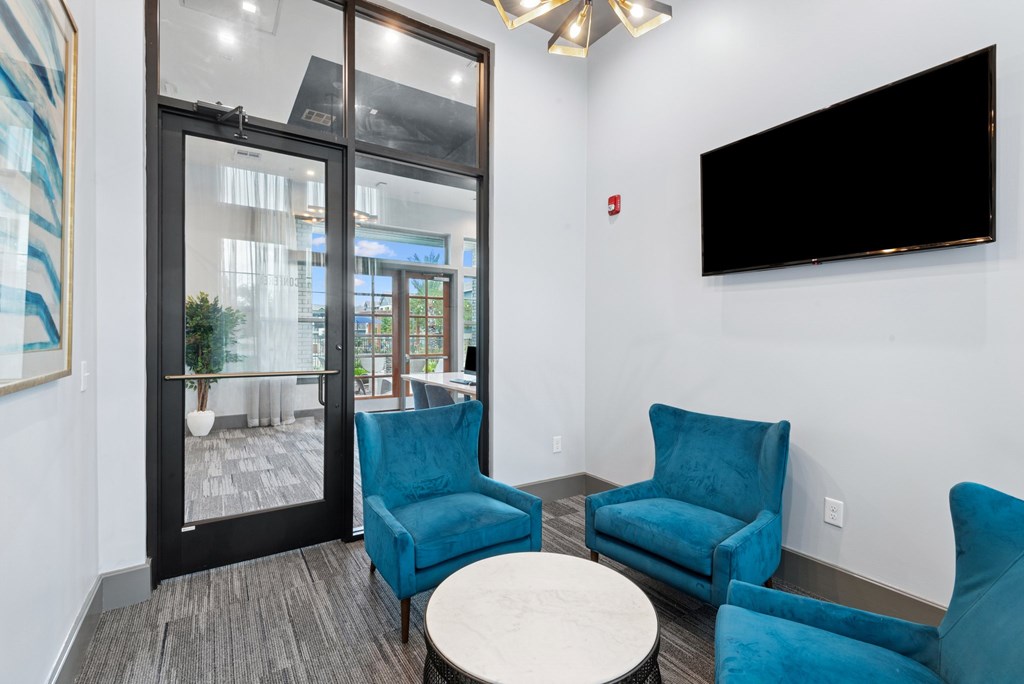 A living room with a black screen on the wall and a glass door leading to a balcony.