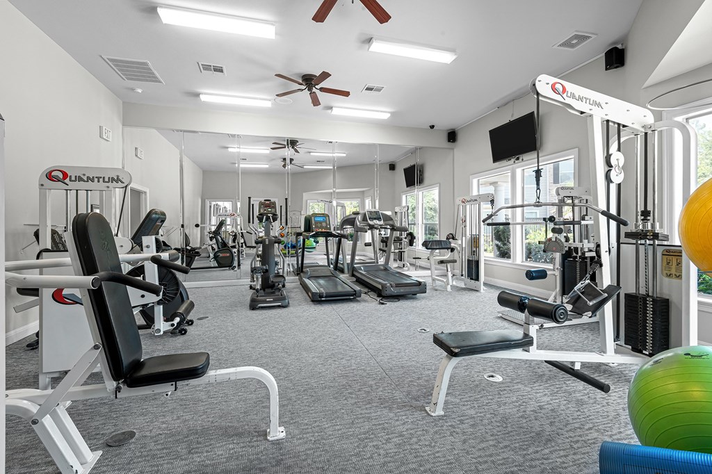 a gym with cardio equipment and weights in a building with windows