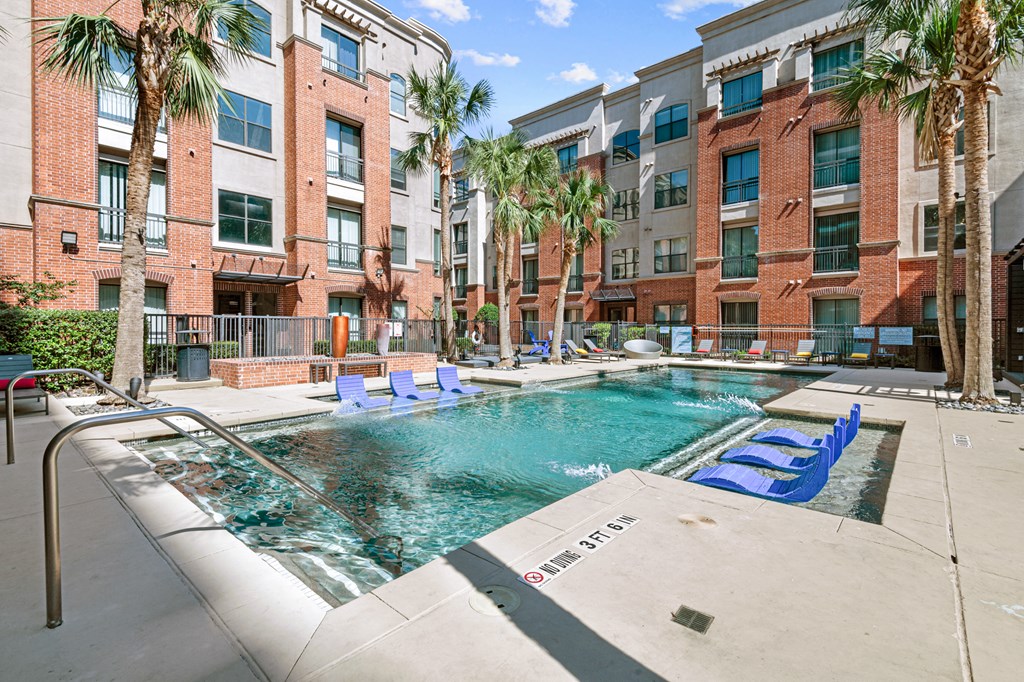 a swimming pool with blue lounge chairs in front of an apartment building