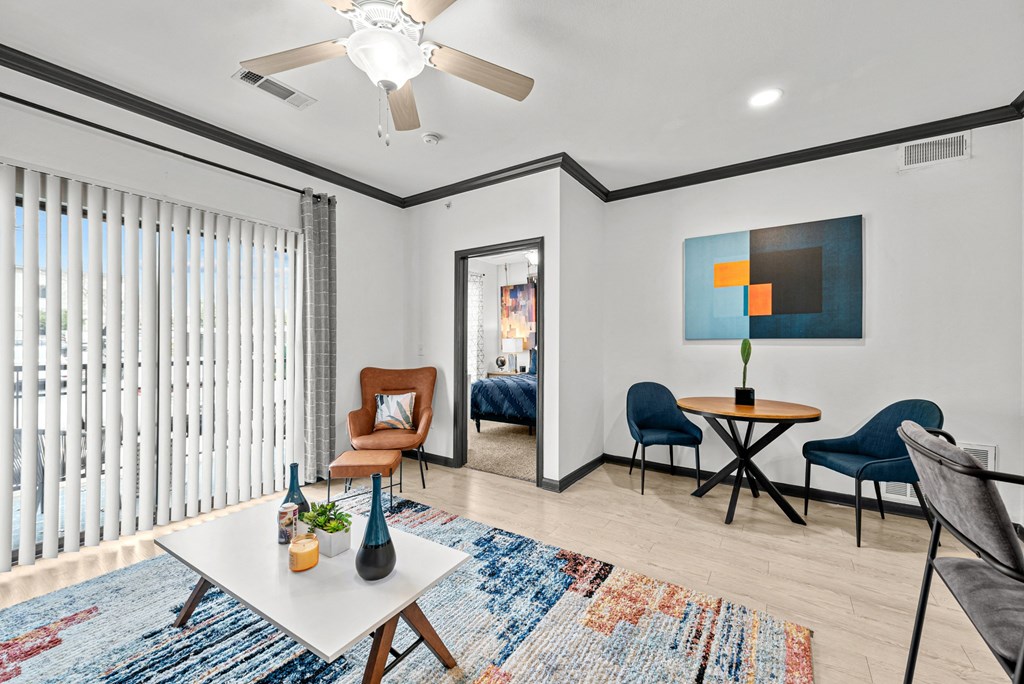 A living room with a white ceiling fan, a blue rug, and a painting on the wall.