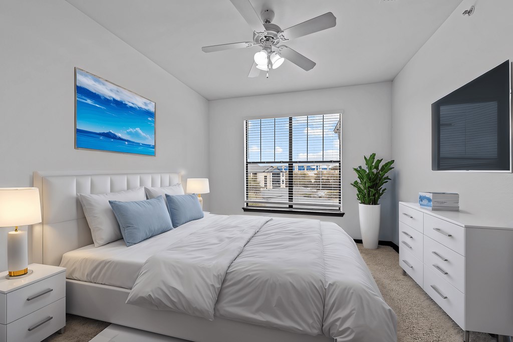A bedroom with a large bed, a ceiling fan, and a painting on the wall.
