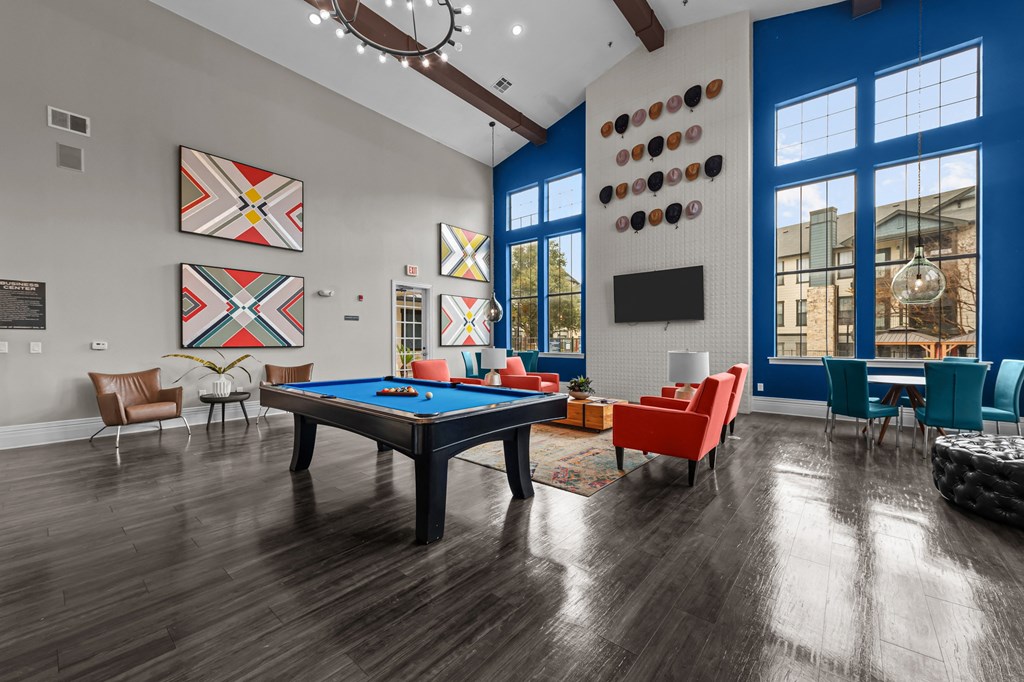 A pool table is surrounded by chairs in a room with wood flooring.