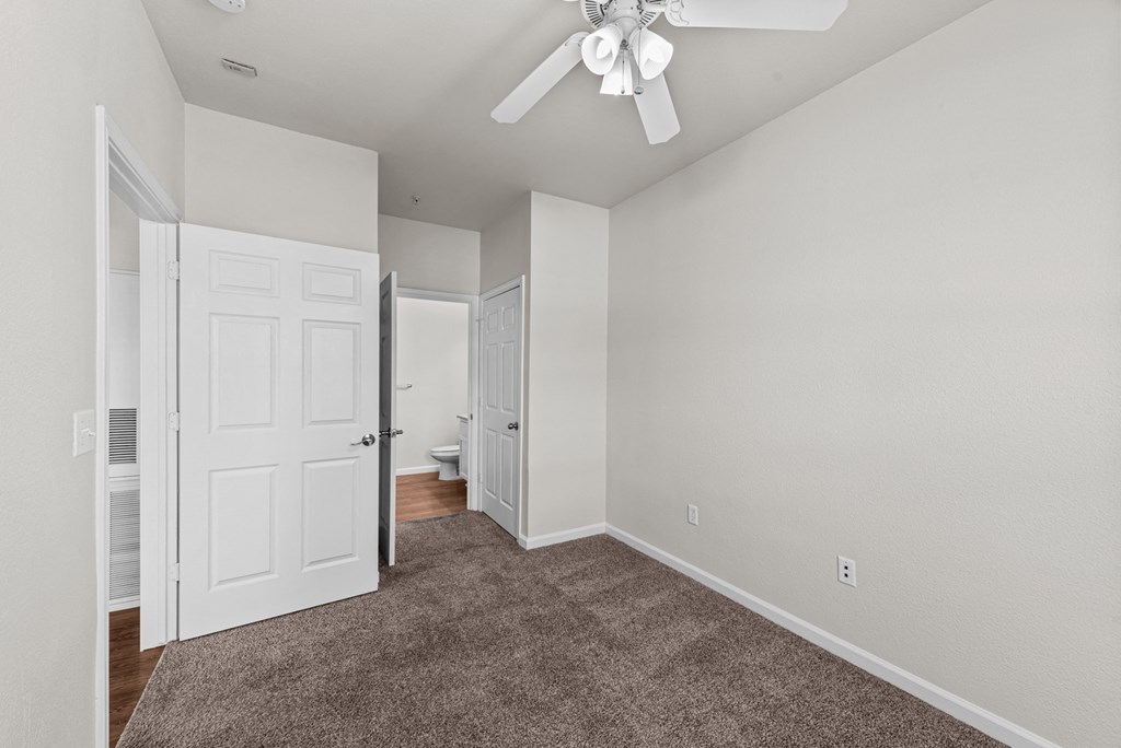 an empty bedroom with a ceiling fan and a door to a bathroom