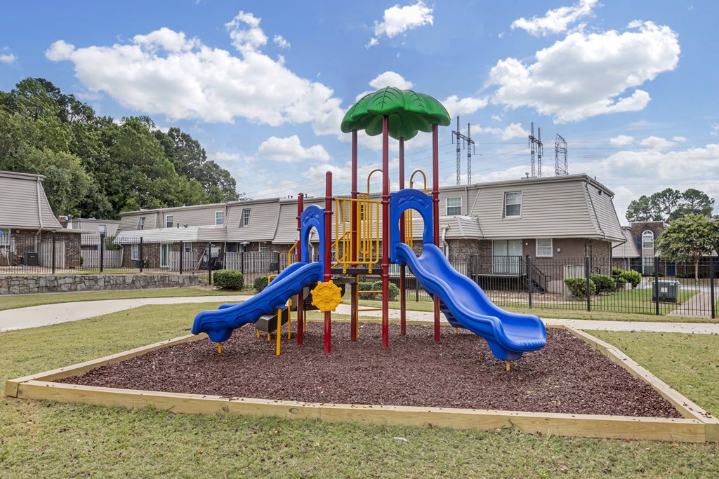 A playground with a blue slide and a green umbrella.