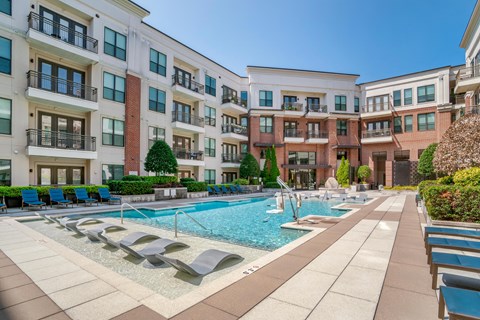 A large swimming pool surrounded by lounge chairs and apartment buildings.