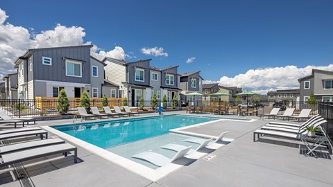 A swimming pool surrounded by lounge chairs and apartment buildings.