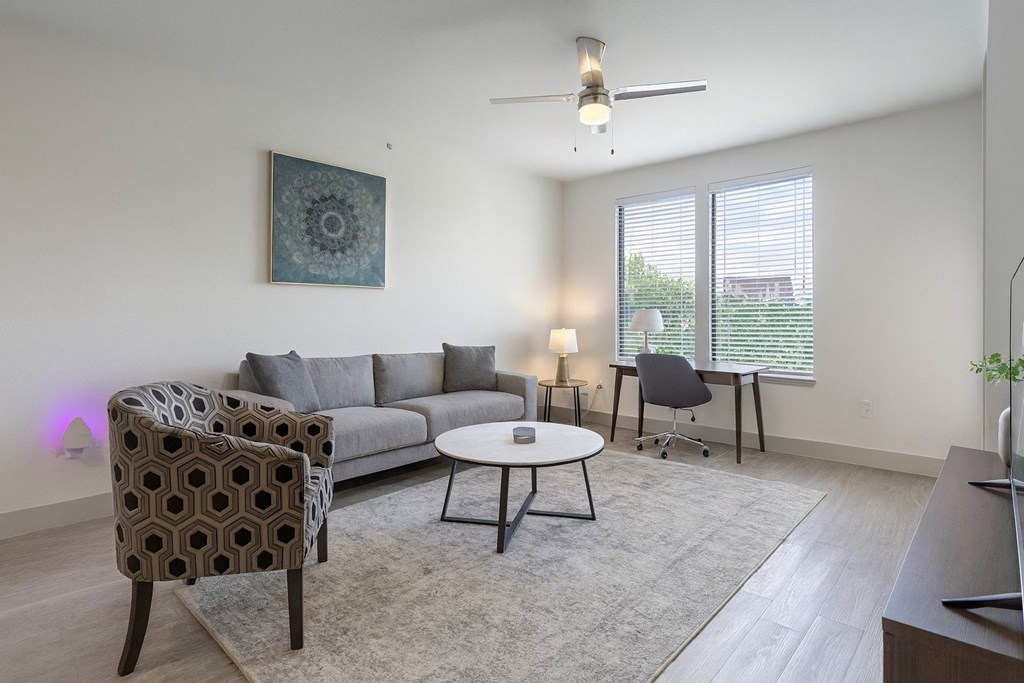 A living room with a grey sofa, a patterned chair, a small table, and a ceiling fan.