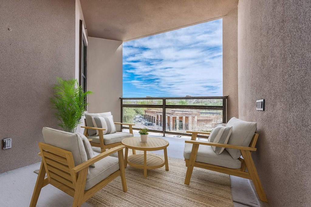 A balcony with two chairs and a table with a view of the sky and buildings.